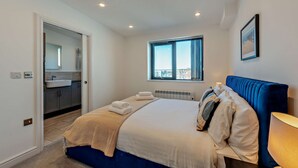 A bedroom with a bed, a window, a radiator, and a view of the city. - Penthouse on the Seafront (Worthing)