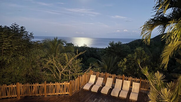 A wooden deck with lounge chairs overlooking a pool and a view of the ocean. - New! Luxurious villa with pool and exceptional view of the Caribbean (Deshaies)