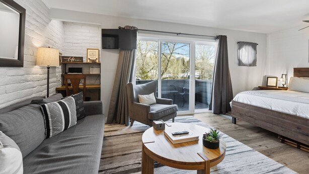Une chambre moderne avec un canapé, un fauteuil, un lit, une petite table et un téléviseur.