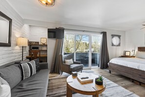 Un dormitorio moderno con sofá, sillón, cama, mesita y televisor.