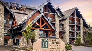 Un immeuble à plusieurs étages avec une façade en pierre, des éléments décoratifs en bois et une enseigne indiquant « GRANDE ROCKIES RESORT, 901, rue Mountain ».