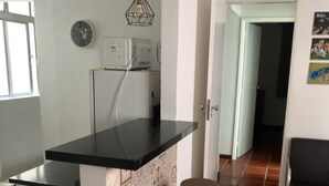 Una cocina con encimera negra, refrigerador, un reloj y un salpicadero con diseño. Hay dos taburetes y una lámpara colgante.