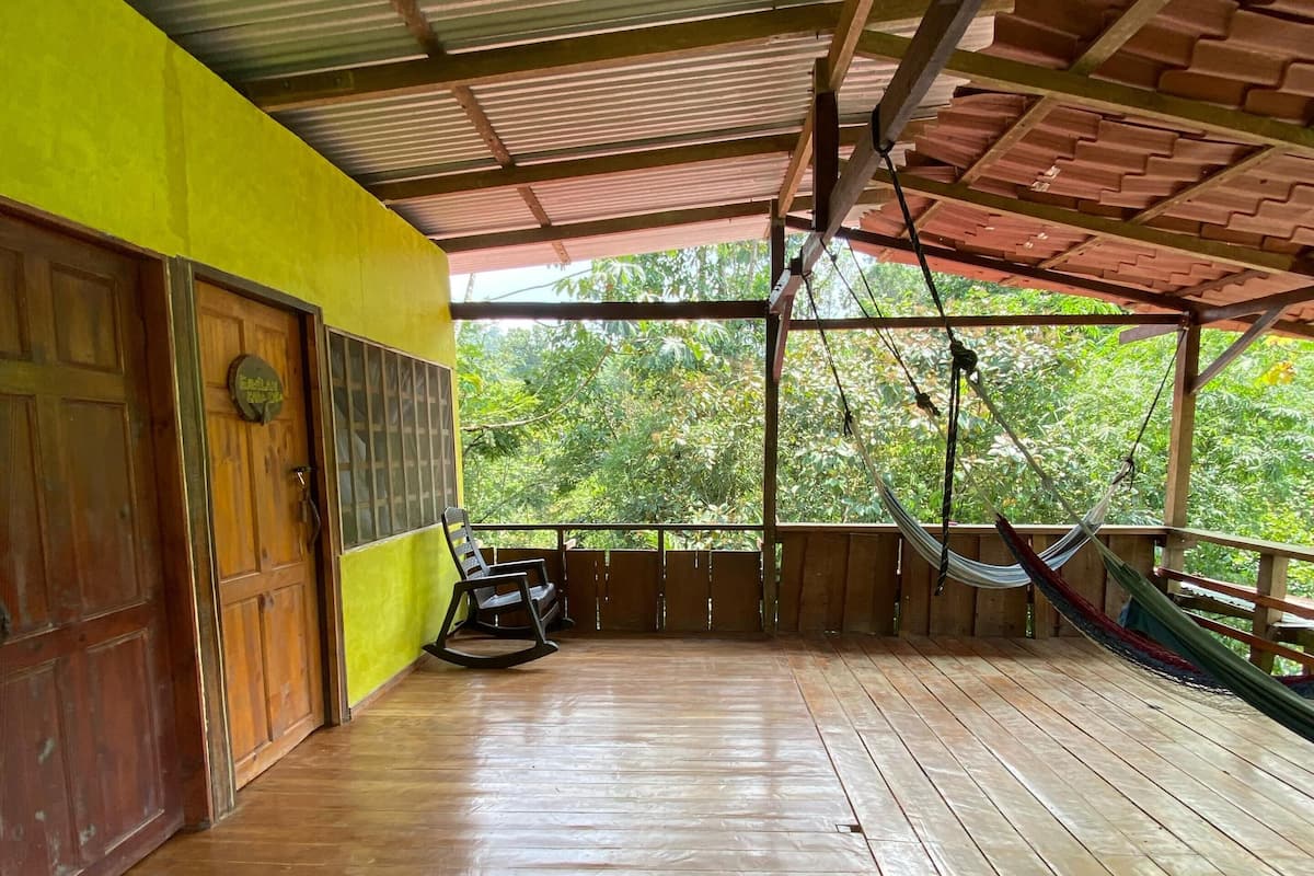 Une terrasse en bois avec un toit en métal, une chaise berçante et un hamac.