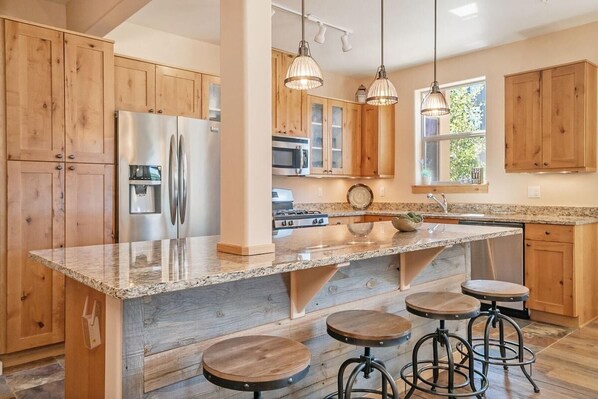 A kitchen with wooden cabinets, stainless steel appliances, a granite countertop, and bar stools.