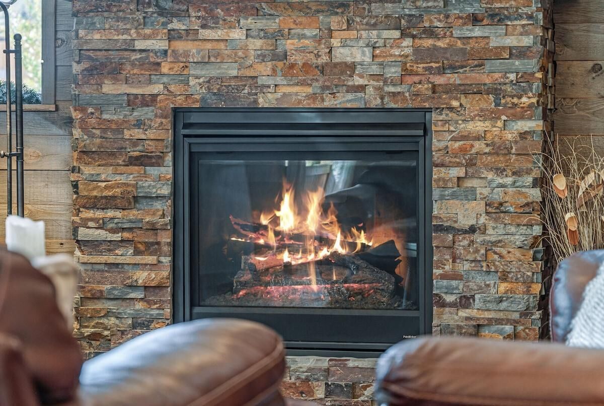 Chimenea con pared de piedra, marco negro y fuego visible.