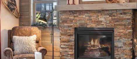 Una sala de estar acogedora con chimenea, un sillón estampado y una lámpara de pie.