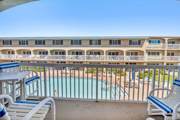 Un balcon d’hôtel donnant sur la piscine, avec des chaises longues et une vue sur l’espace piscine.