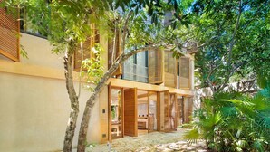 Ein modernes Haus mit überdachter Terrasse, Holzhörnern und einem Garten mit tropischen Pflanzen.