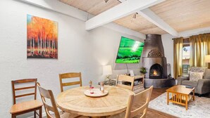Un comedor con una mesa redonda de madera y sillas, un televisor de pantalla plana montado en la pared, una chimenea y un sofá en la sala de estar.