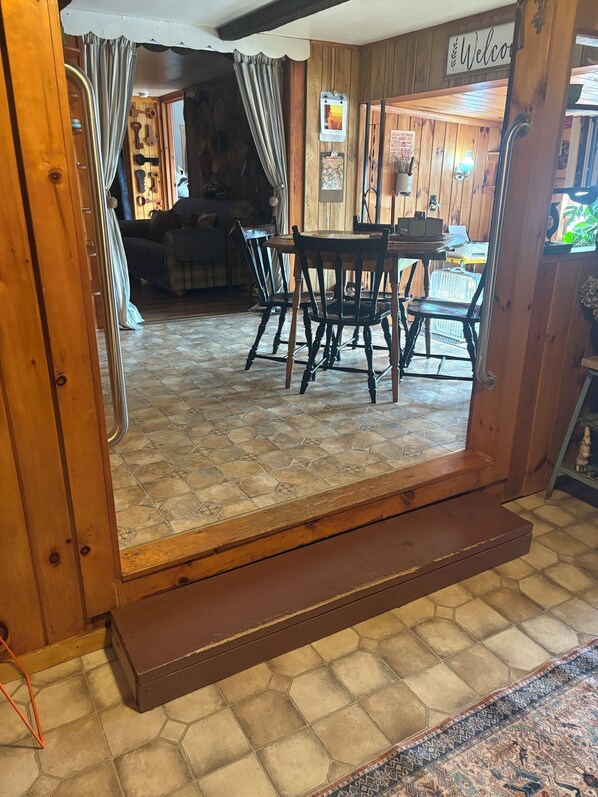 A wooden interior with a dining table and chairs, a staircase, and a 'Welcome' sign.