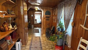 Een houten interieur met een zeshoekige tegelvloer, een witte stoel, een rode emmer en een potplant.