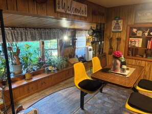 Un intérieur en bois avec une table à manger, des chaises jaunes et une pancarte « Bienvenue ».