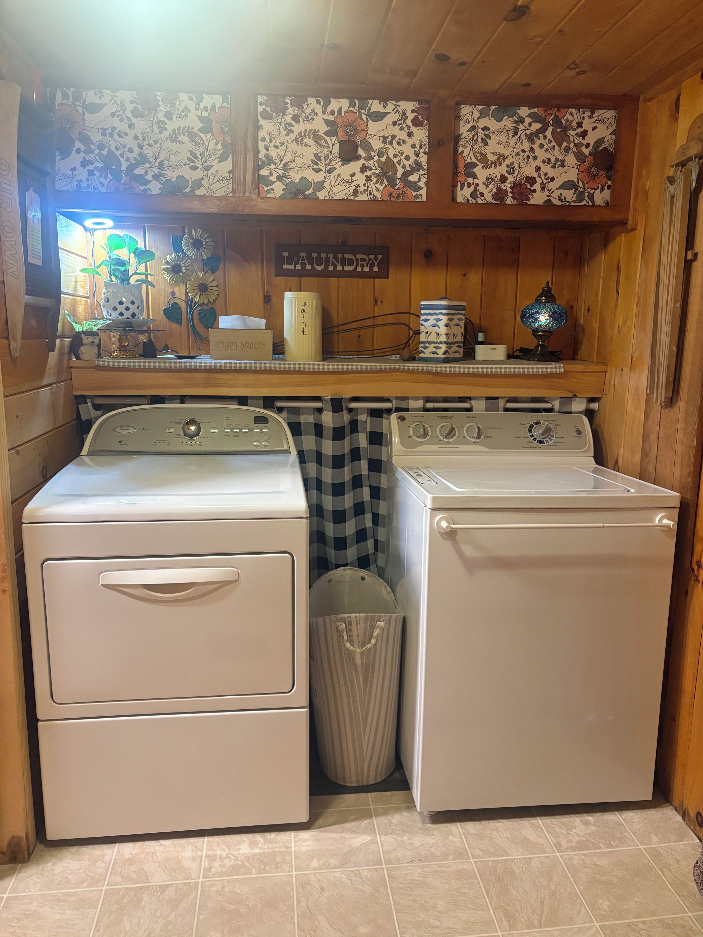 A laundry room with two white washers and dryers, a trash can, and a shelf with a 'laundry' sign.