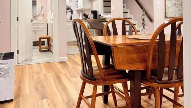 A modern kitchen with wooden cabinets, a dining table with chairs, and a staircase leading to another level.