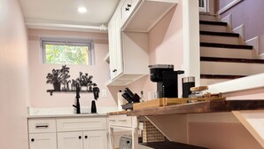 A modern kitchen with white cabinets, a stainless steel coffee machine, and a built-in oven.