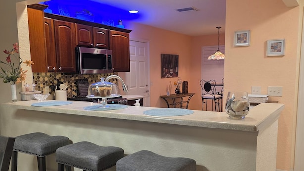 A modern kitchen with a central island, bar stools, wooden cabinets, and a blue-lit ceiling.