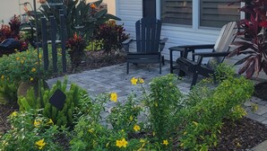 A residential house with a patio area featuring a table and chairs, surrounded by a garden with various plants and flowers.