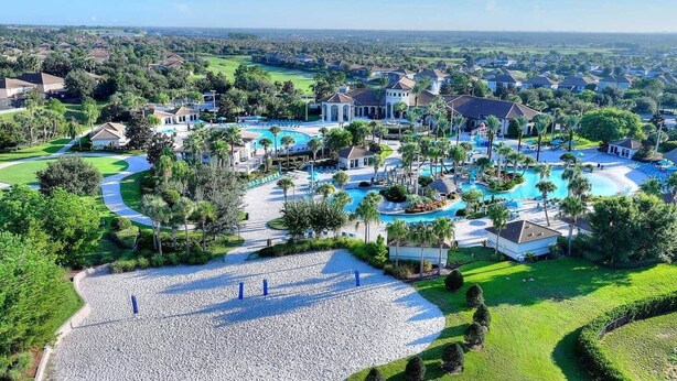 Ein Luftbild zeigt ein Resort mit mehreren Schwimmbecken, einer großzügigen Grünanlage und umgebenden Wohngebäuden.