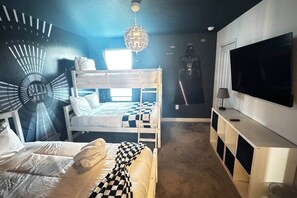 Une chambre avec un lit superposé, une couverture à carreaux, un téléviseur fixé au mur et une affiche de Dark Vador.