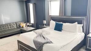 Ein modernes Schlafzimmer mit einem großen Bett, einem grauen Sofa und einem Nachttisch mit einer Lampe.