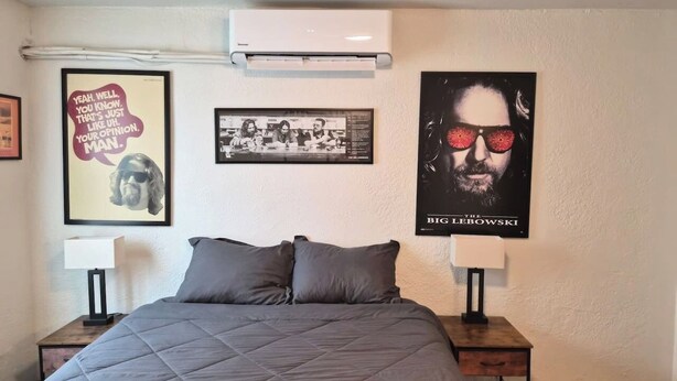 Quarto com uma cama grande, duas mesas de cabeceira, um ar condicionado fixado na parede e três quadros na parede.