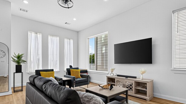 A modern living room with a black leather sofa, two armchairs, a coffee table, and a flat-screen TV mounted on the wall. - Play, work, relax, repeat: a sleek 3Bd/3.5Ba retreat near Houston’s top hubs.” (Houston)