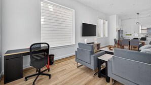 A modern living room with a grey sofa, a black office chair, a wooden desk, and a flat-screen TV mounted on the wall. - Play, work, relax, repeat: a sleek 3Bd/3.5Ba retreat near Houston’s top hubs.” (Houston)
