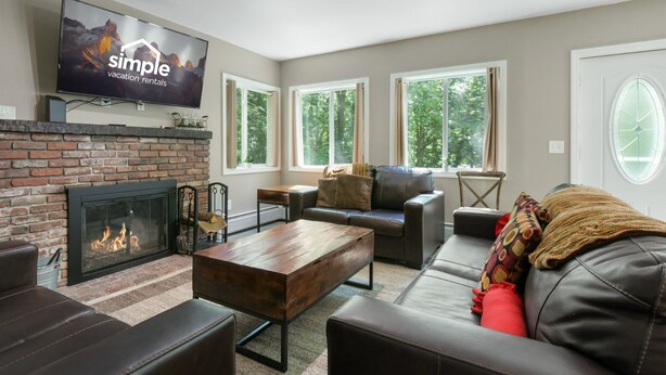 A modern living room with a fireplace, leather sofas, a coffee table, and a flat-screen TV mounted on the wall.