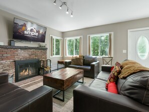 Una sala de estar moderna con chimenea, sofás de cuero, una mesa de centro y un televisor de pantalla plana montado en la pared.