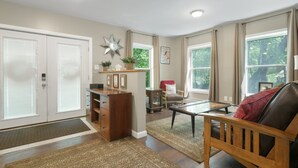 A spacious living area with a wooden bench, a coffee table, and a fireplace. There are two doors with frosted glass panels and a star-shaped mirror on the wall.