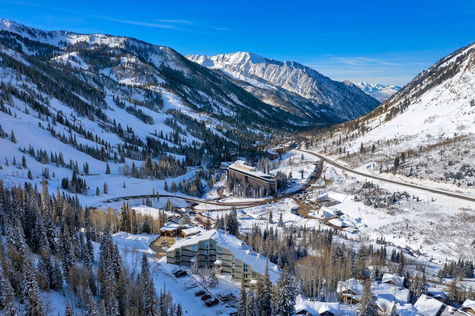 A snow-covered mountain resort with a ski lift, buildings, and a road winding through the landscape.
