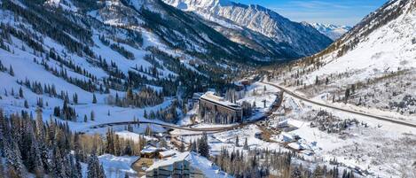 A snow-covered mountain resort with a ski lift, buildings, and a road winding through the landscape.