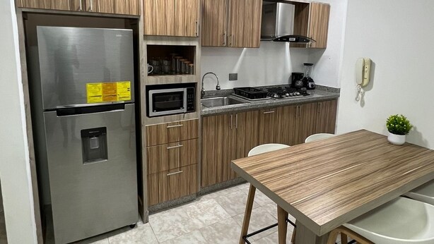 A modern kitchen with a stainless steel refrigerator, wooden cabinets, a microwave, and a gas stove.