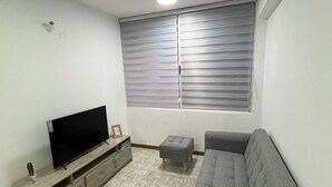A living room with a flat-screen TV, grey sofa, and a small ottoman.