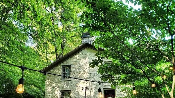 Una casa in pietra con una porta rossa, immersa nel verde e illuminata da luci decorative.
