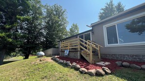 A house with a stone foundation, a wooden deck, and a large window. - Beautiful Lakefront Escape with Private Dock & Wildlife Views (Eau Galle)