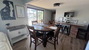 Un comedor con una mesa de madera, sillas y una zona de cocina con salpicadero de ladrillo.