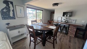 Uma sala de jantar com mesa de madeira, cadeiras e uma cozinha com revestimento de tijolos.