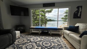 A living room with a large window overlooking a lake, a patterned rug, and a couch with pillows. - Beautiful Lakefront Escape with Private Dock & Wildlife Views (Eau Galle)