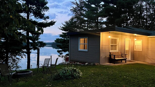 A small cabin with a porch, a bench, and a view of a lake. - Beautiful Lakefront Escape with Private Dock & Wildlife Views (Eau Galle)