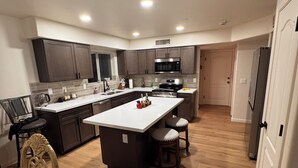 Une cuisine moderne dotée d’un îlot central, de meubles de couleur sombre, d’appareils électroménagers en acier inoxydable et d’un plancher en bois.