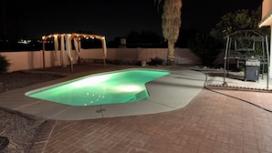 Une piscine dotée d’un jacuzzi intégré, entourée d’un patio agrémenté d’une pergola et d’un barbecue.