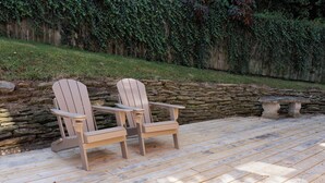 Twee Adirondack stoelen op een houten terras, met een stenen muur en een grasveld achtergrond.