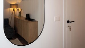 Une pièce avec une porte blanche, un miroir rond, une armoire en bois, une lampe et des tableaux encadrés accrochés au mur.