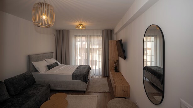 Une chambre moderne avec un lit, un canapé, une commode en bois et un grand miroir.