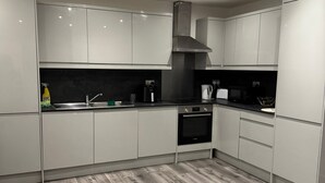 A modern kitchen with white cabinets, a stainless steel range hood, a built-in oven, and a microwave.