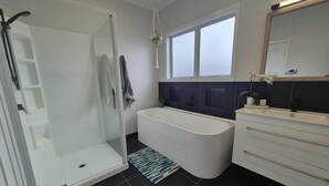 A modern bathroom with a glass shower enclosure, a freestanding bathtub, and a vanity with a mirror.