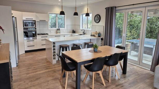 A modern kitchen with a central island, wooden flooring, and black chairs around a wooden dining table.
