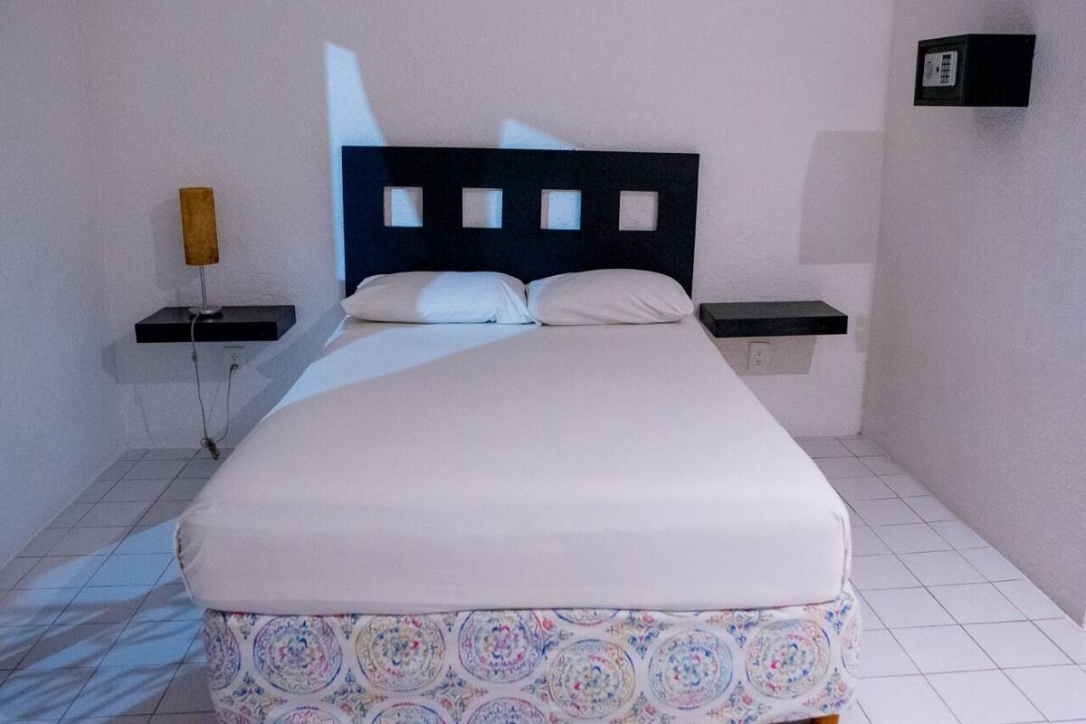 A bedroom with a bed, two bedside tables, and a wall-mounted light fixture.