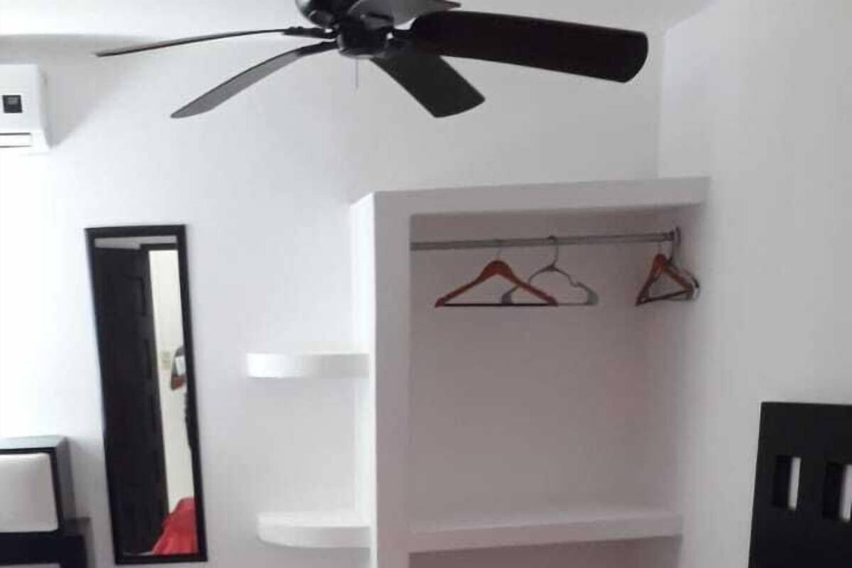 A bedroom with a red bed, a ceiling fan, a white wardrobe, and a mirror.